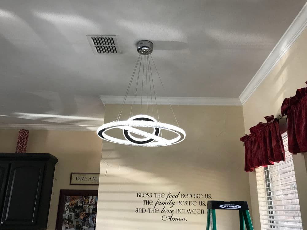 Modern circular chandelier with adjustable cords hanging in a well-lit room.