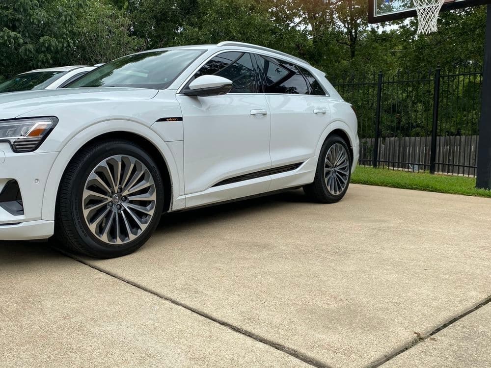 White luxury SUV parked on concrete driveway next to a basketball hoop and greenery.