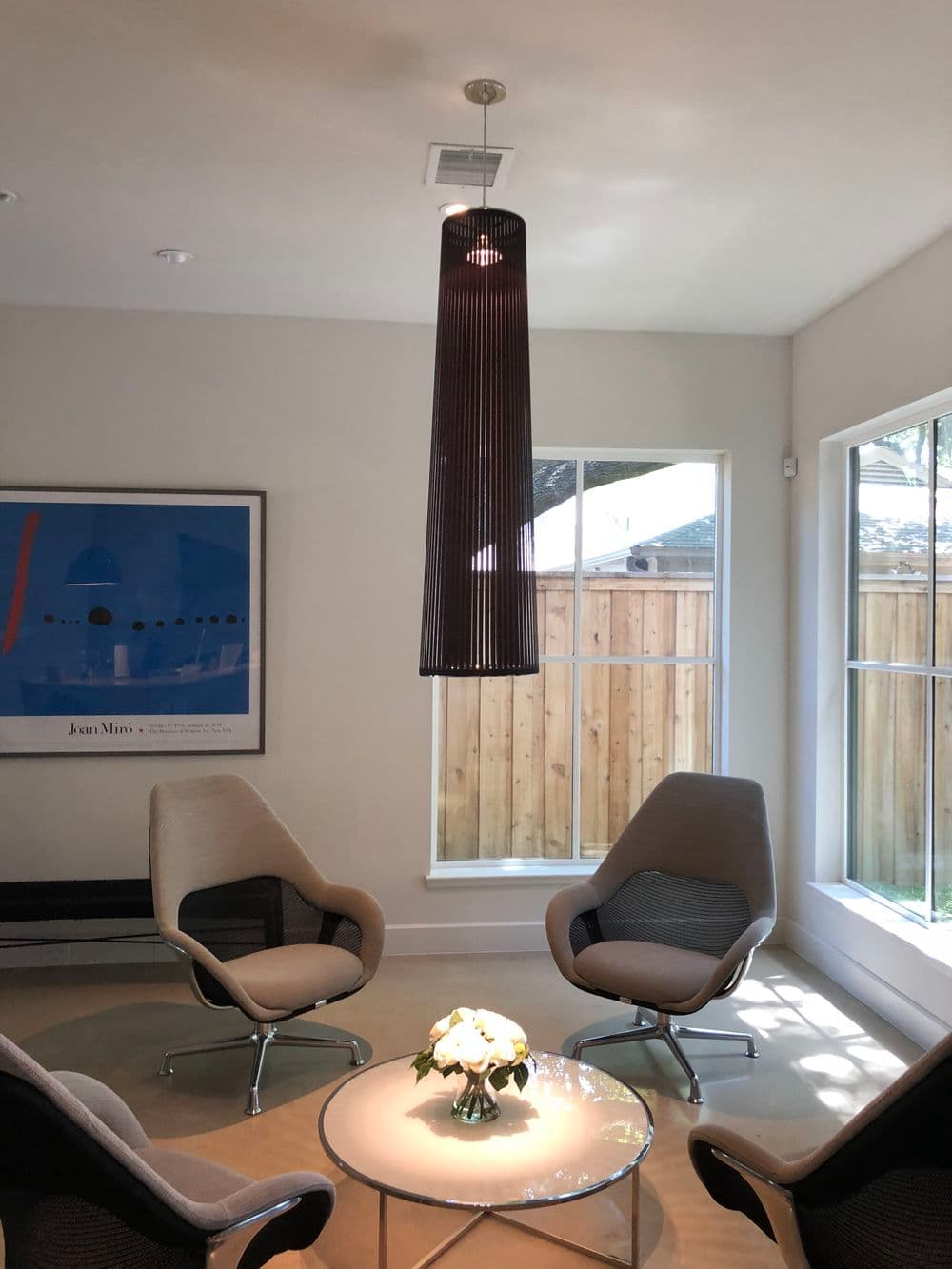Modern living room with sleek chairs, round glass table, and unique pendant lamp. Natural light.