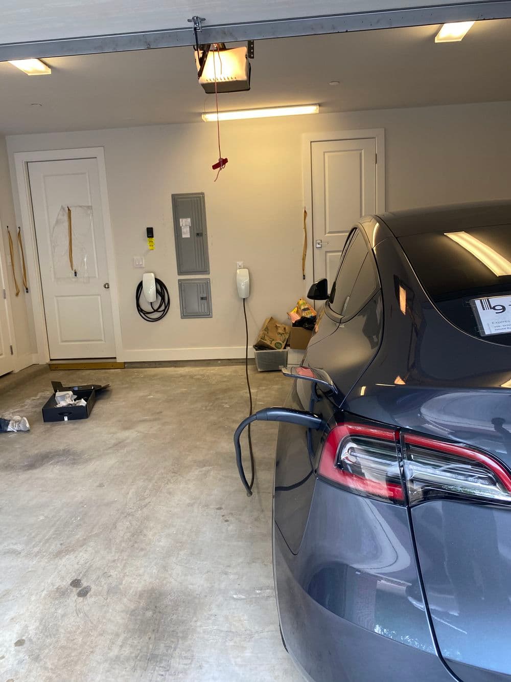 Electric car charging in a modern garage with utility panel and tools visible.