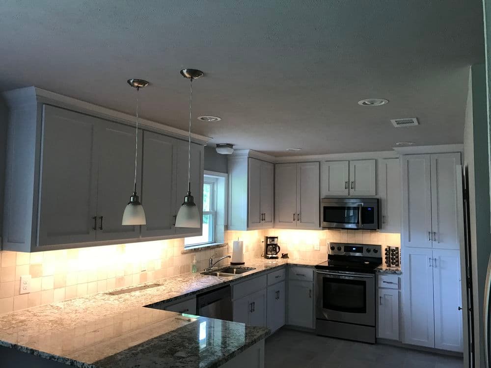 Modern kitchen with gray cabinets, granite countertops, stainless steel appliances, and pendant lights.