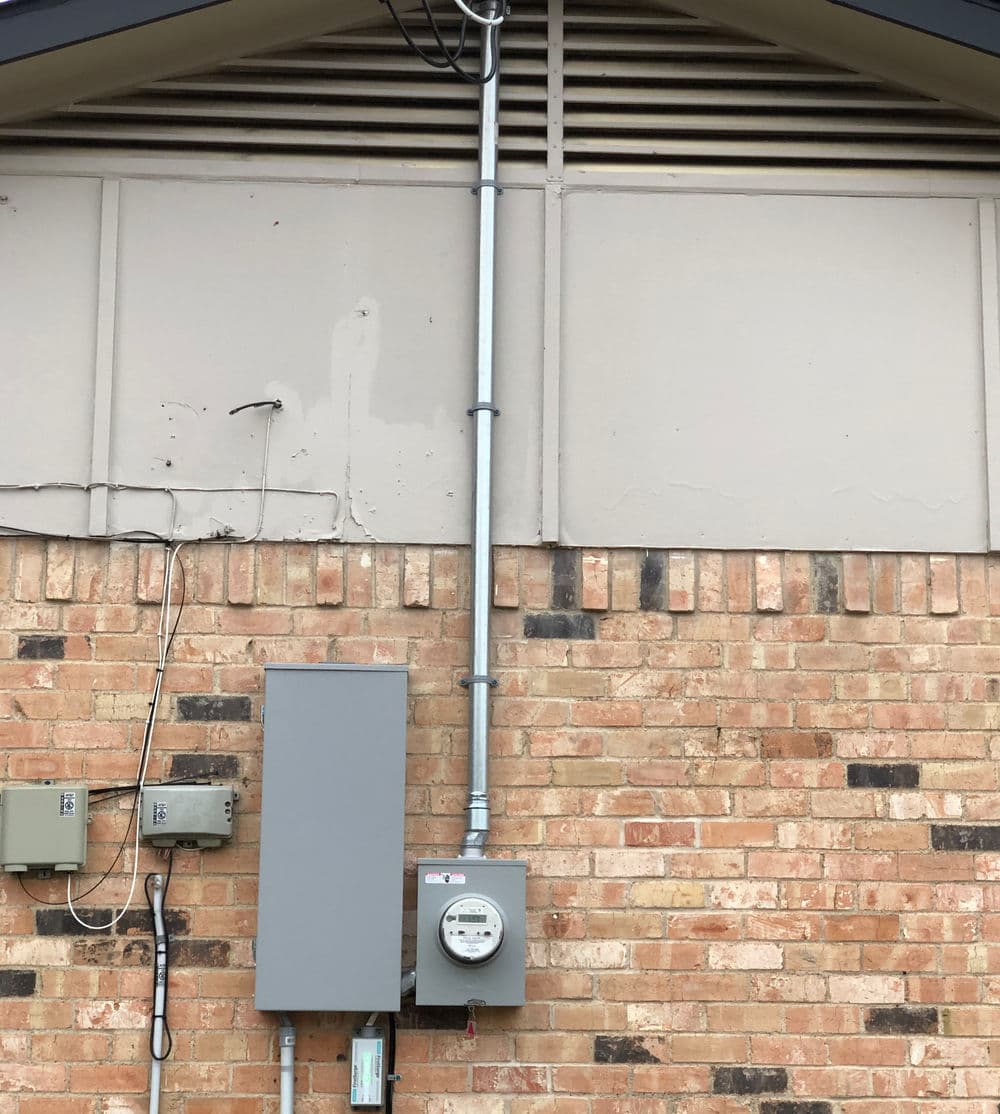 Electricity meter and enclosure mounted on a brick wall, with utility connections visible.